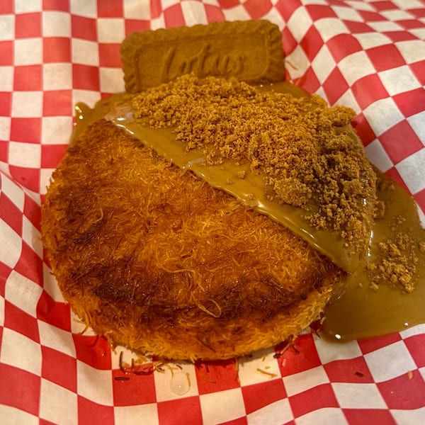 Golden Chicken's kunafa dessert, topped with Lotus Biscoff spread, crumbs, and a cookie, on checkered paper.