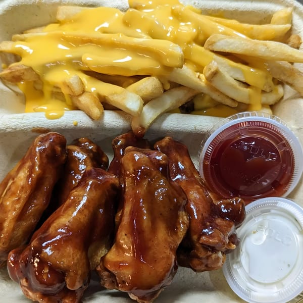 Cheesy fries and BBQ chicken wings with ketchup and sauce in a takeout container.