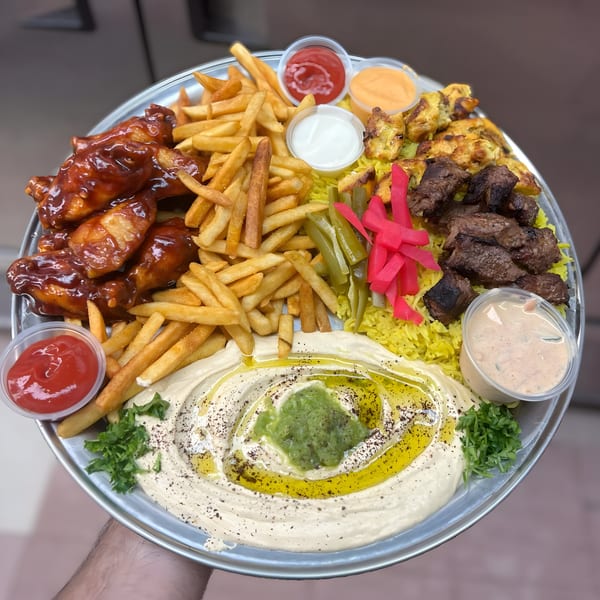 A large platter of Mediterranean food with chicken wings, fries, hummus, rice, and various meats.