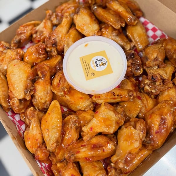 Golden Chicken wings in a box with a side of dipping sauce, on a checkered napkin.