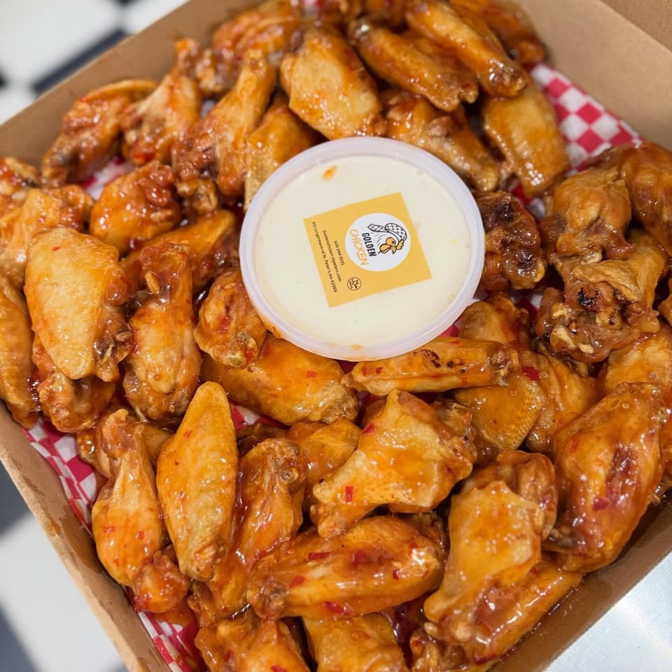 Golden Chicken wings in a box with a side of dipping sauce, on a checkered napkin.