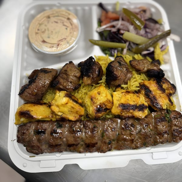 Golden Chicken's Mediterranean platter with grilled meats, yellow rice, salad, and sauce in a takeout container.