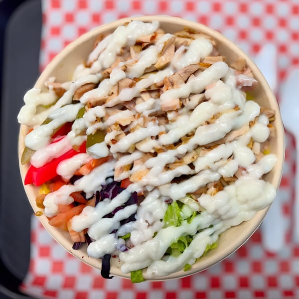 Golden Chicken's Mediterranean bowl with chicken, fresh vegetables, and white sauce on a red and white checkered tray.