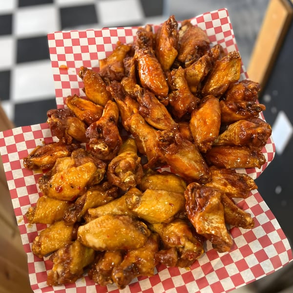 A large basket of Golden Chicken's glazed chicken wings on red and white checkered paper.