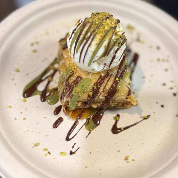 Golden Chicken's baklava dessert with ice cream, pistachio, and chocolate drizzle on a white plate.